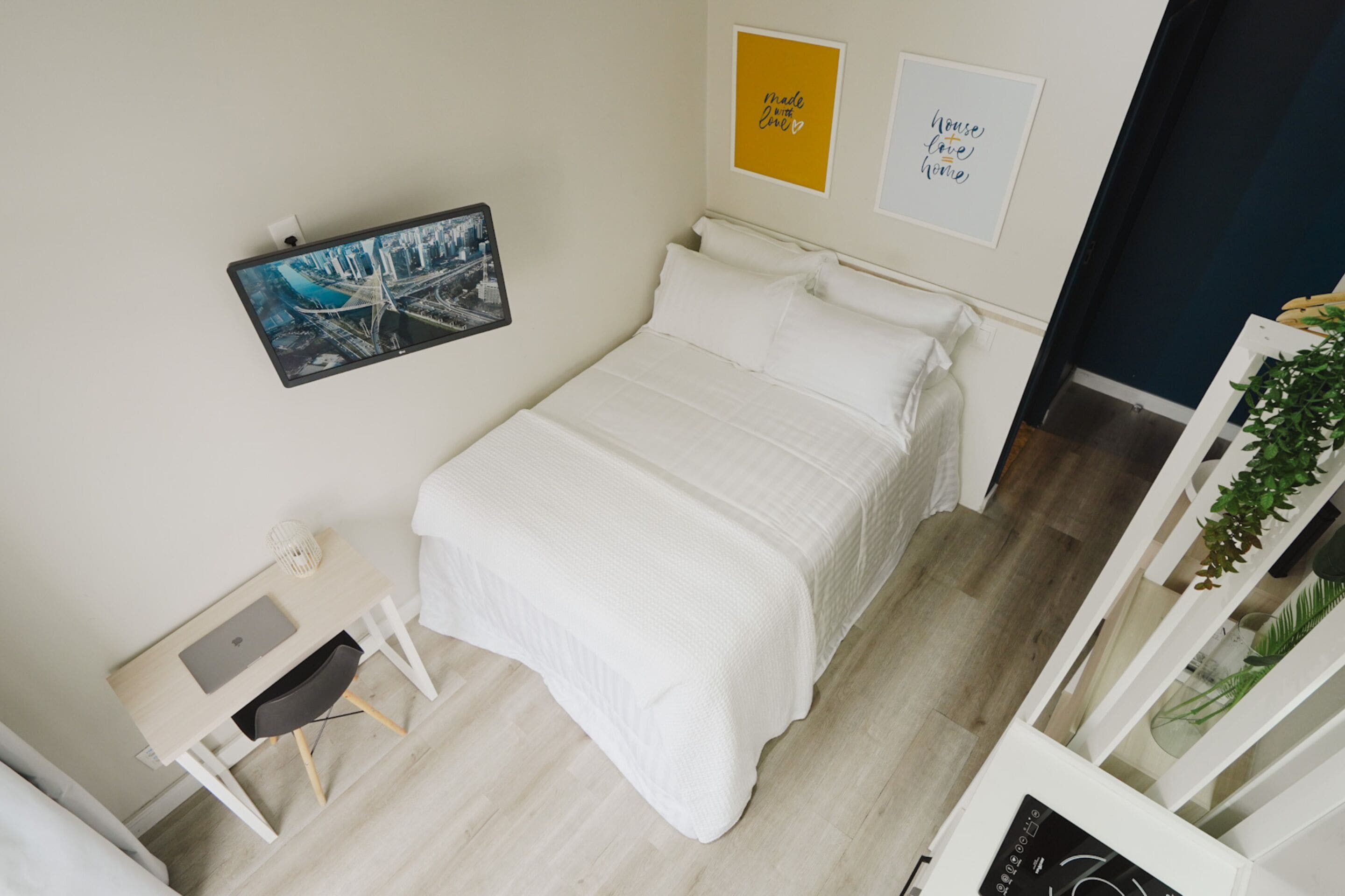 Une chambre bien rangée, avec un lit, un bureau et une chaise. Deux tableaux encadrés sont accrochés au mur.