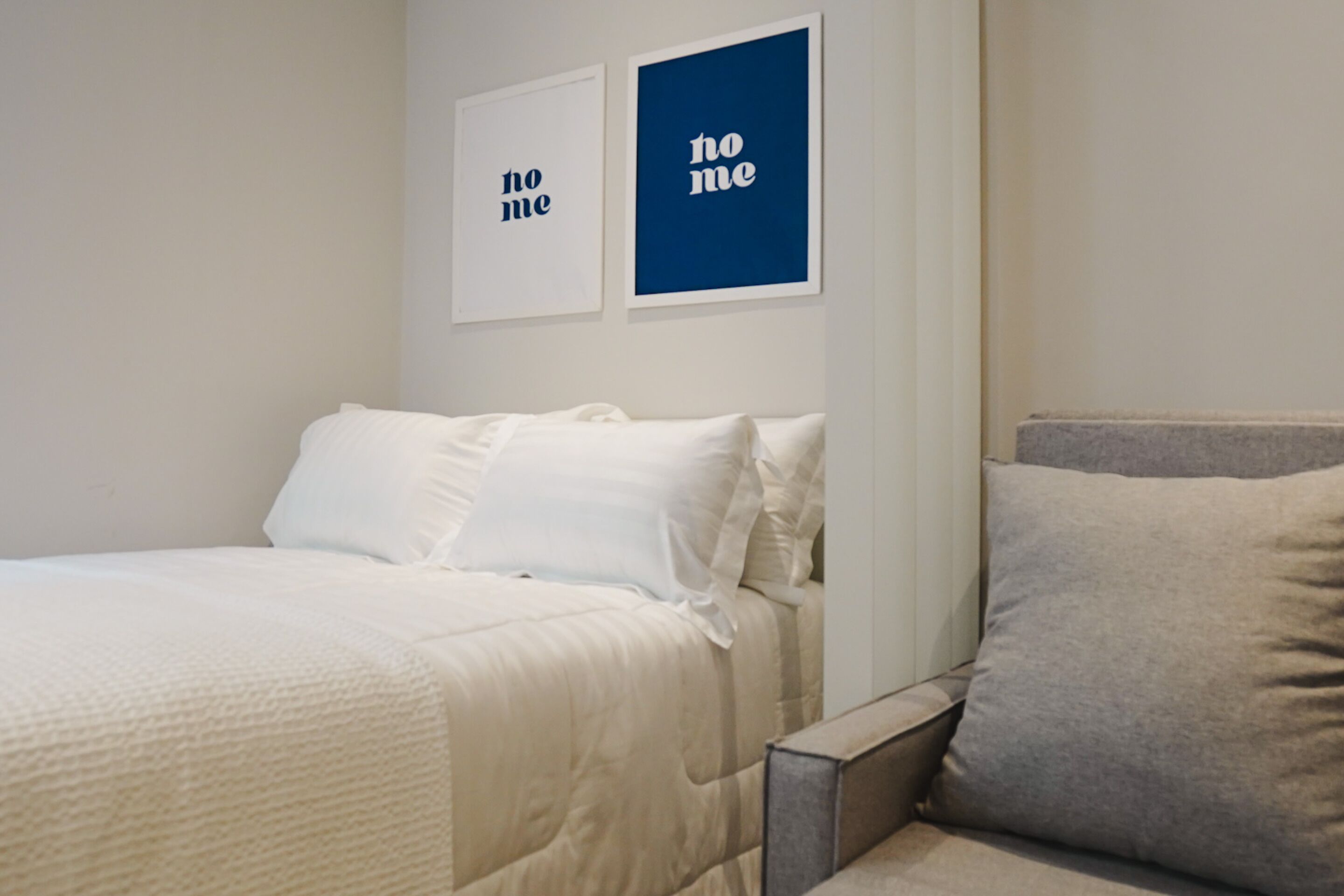 A neatly made bed with white bedding, a grey pillow, and two framed pictures on the wall.