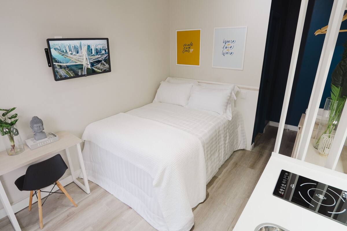 Ein modernes Hotelzimmer mit Bett, Schreibtisch und Stuhl. An der Wand hängen zwei gerahmte Bilder, auf dem Schreibtisch steht eine kleine Buddha-Statue und eine Pflanze.