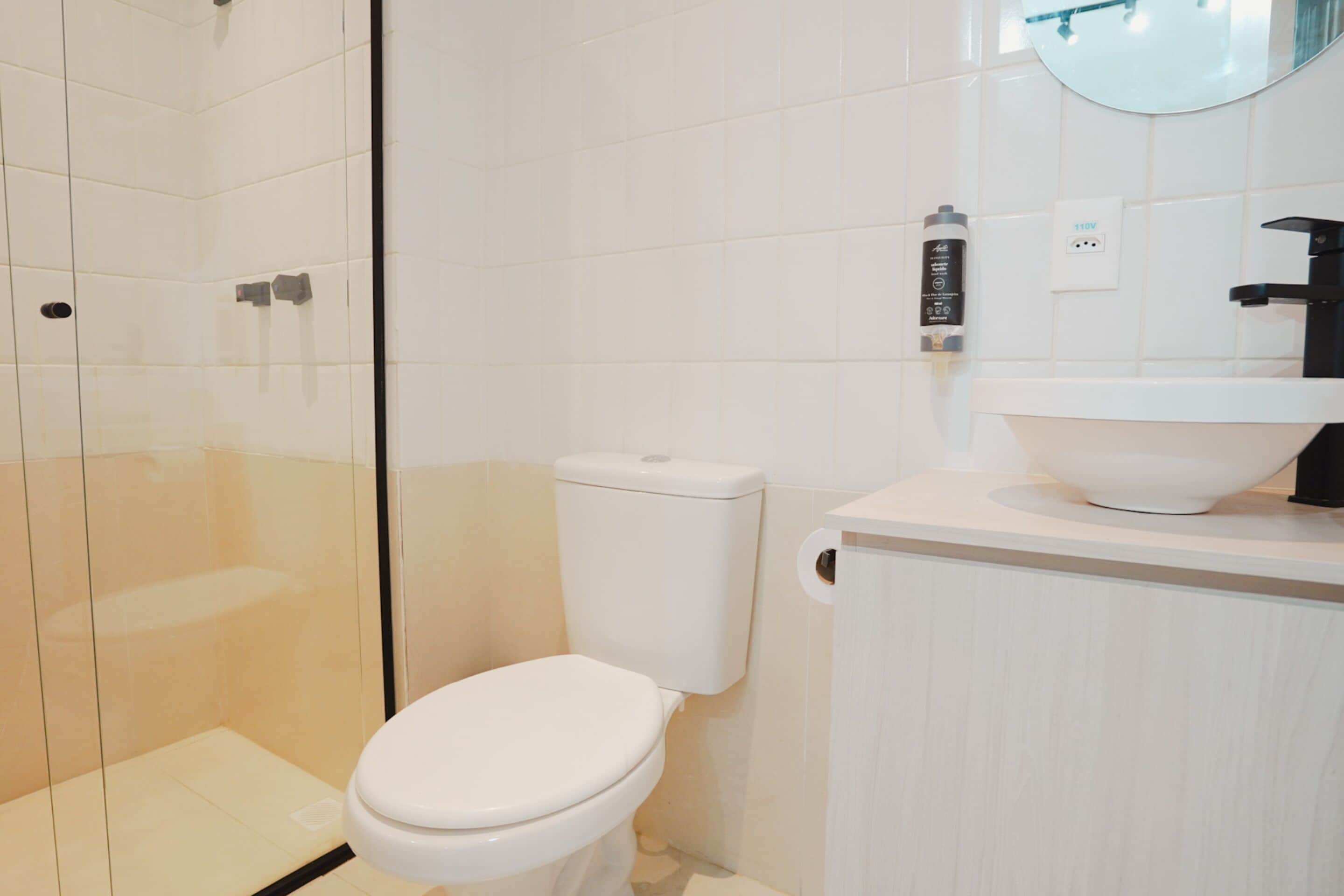 Egy modern fürőszoba üveg válaszfallal ellátott zuhanyzóval, fehér WC-vel és egy mosdókagylóval, melynek felett tükör található.