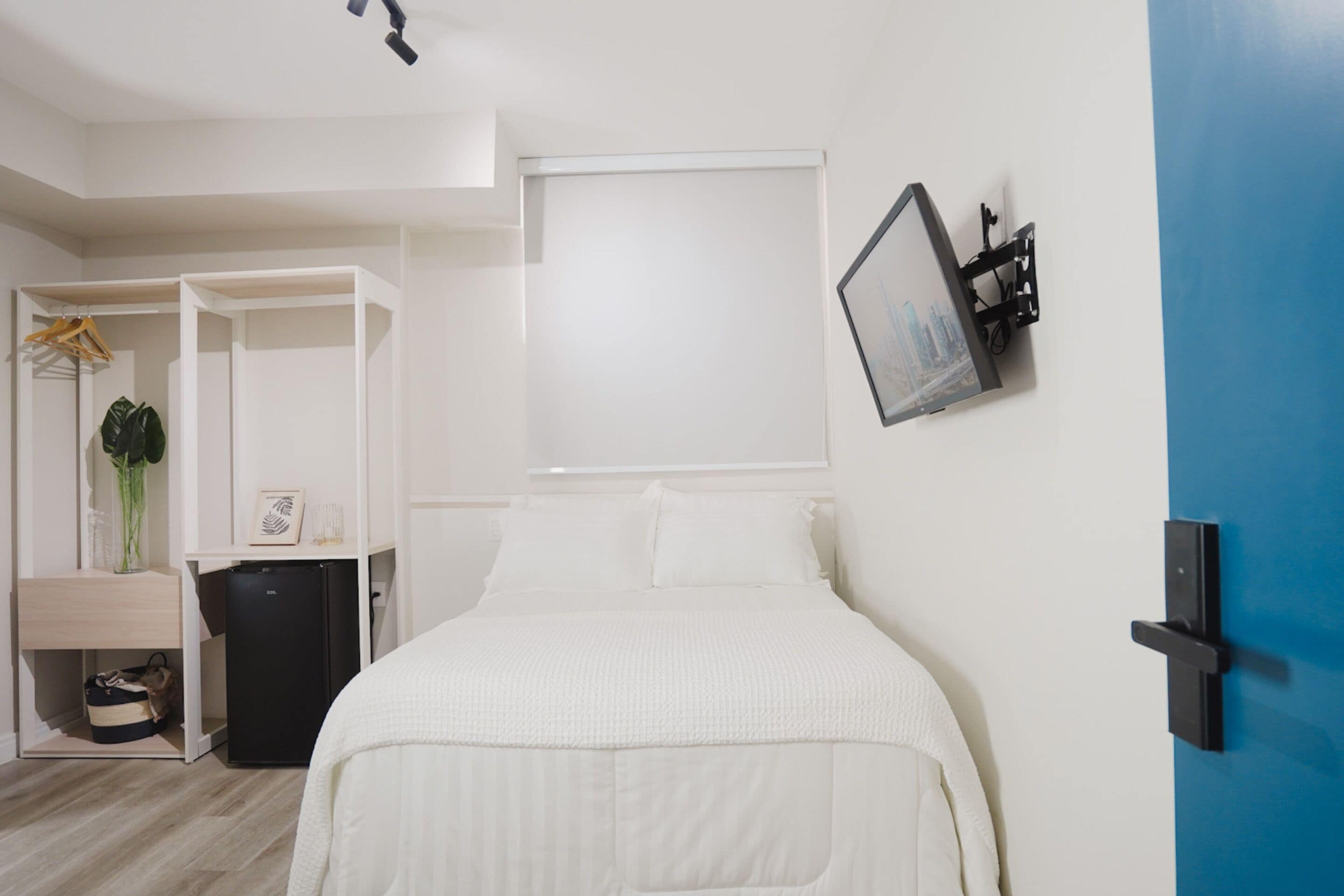 A modern bedroom with a bed, a wardrobe, a small desk, and a door with a picture frame.