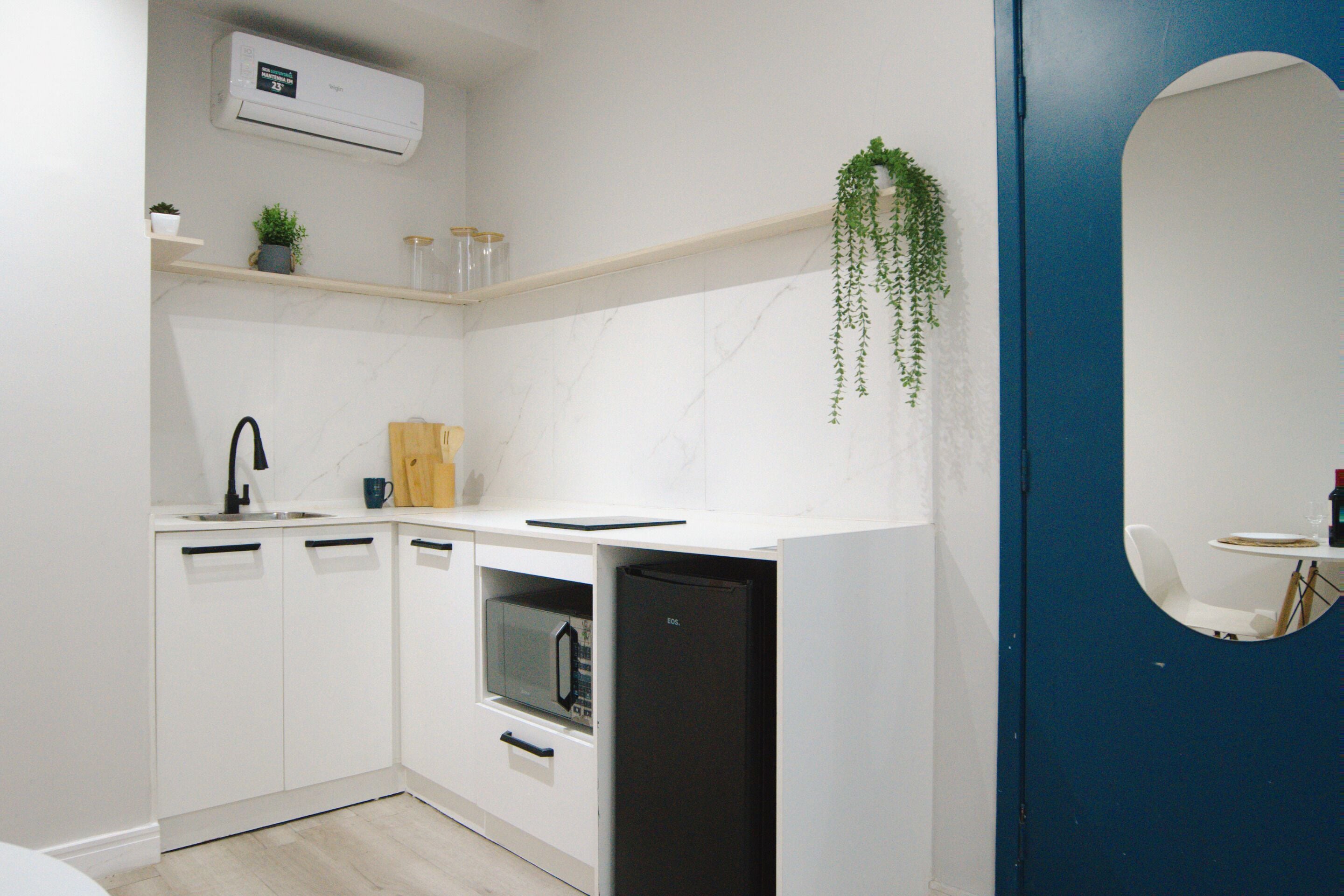 Una cocina moderna con armarios blancos, horno empotrado, microondas y una planta colgante.