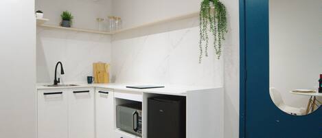 Une cuisine moderne avec des meubles blancs, un four encastré, un micro-ondes et une plante suspendue.