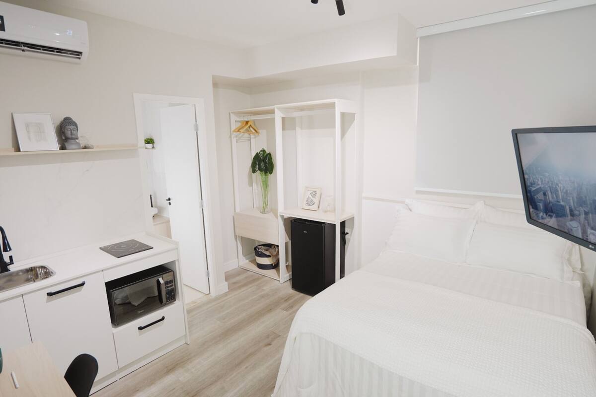 Ein kleines Hotelzimmer mit Kochnische, Bett, Fernseher und Kleiderschrank.