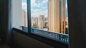 A view from a window with a blue balcony railing, overlooking a cityscape with tall buildings and a clear sky. - Apê Metrô Paraíso (São Paulo)
