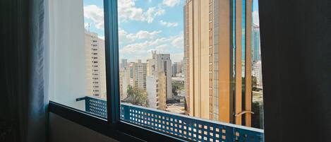 Vista desde una ventana con barandal azul, sobre un paisaje urbano de edificios altos y cielo despejado.