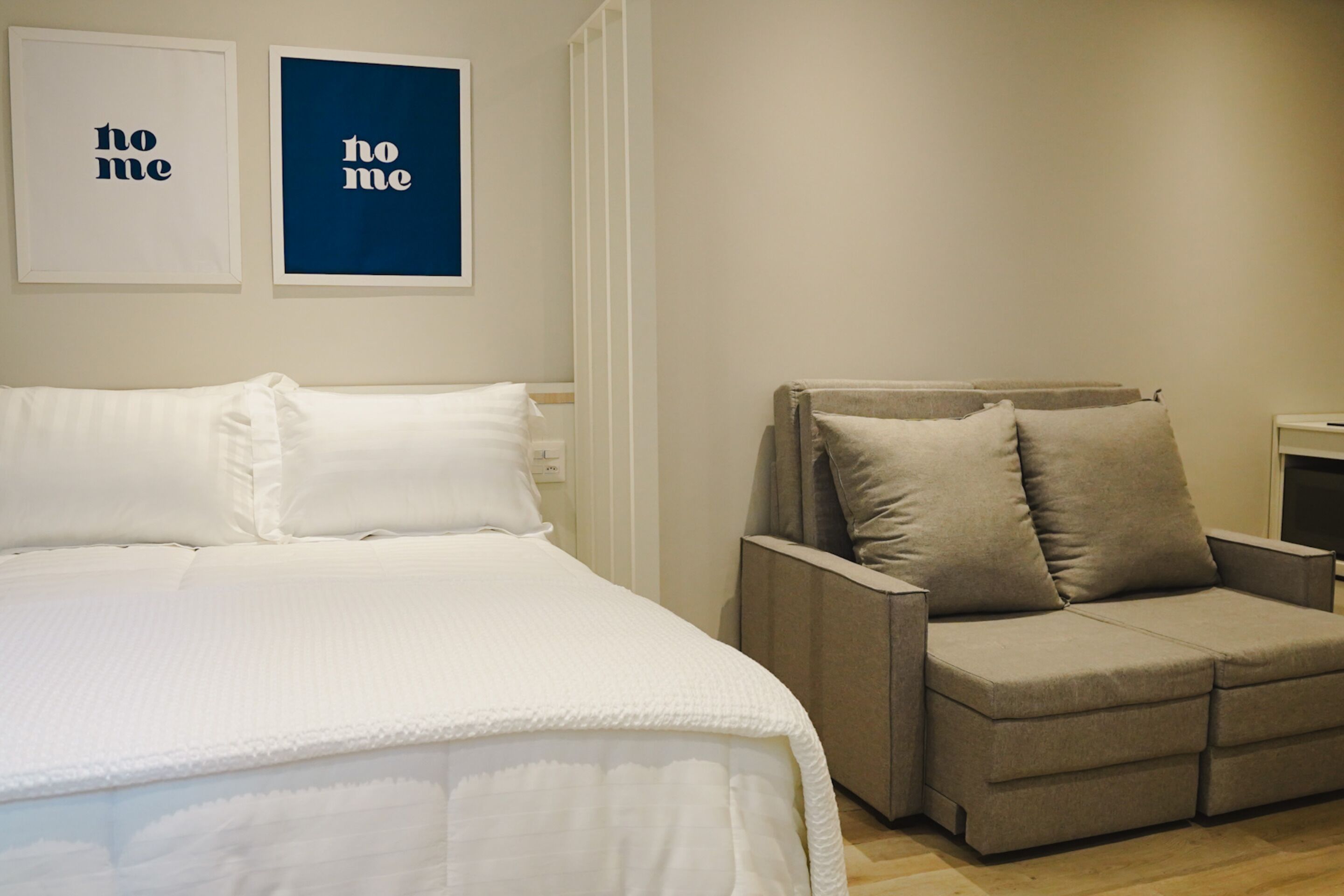 Un dormitorio con una cama, un sofá gris y dos cuadros en la pared.