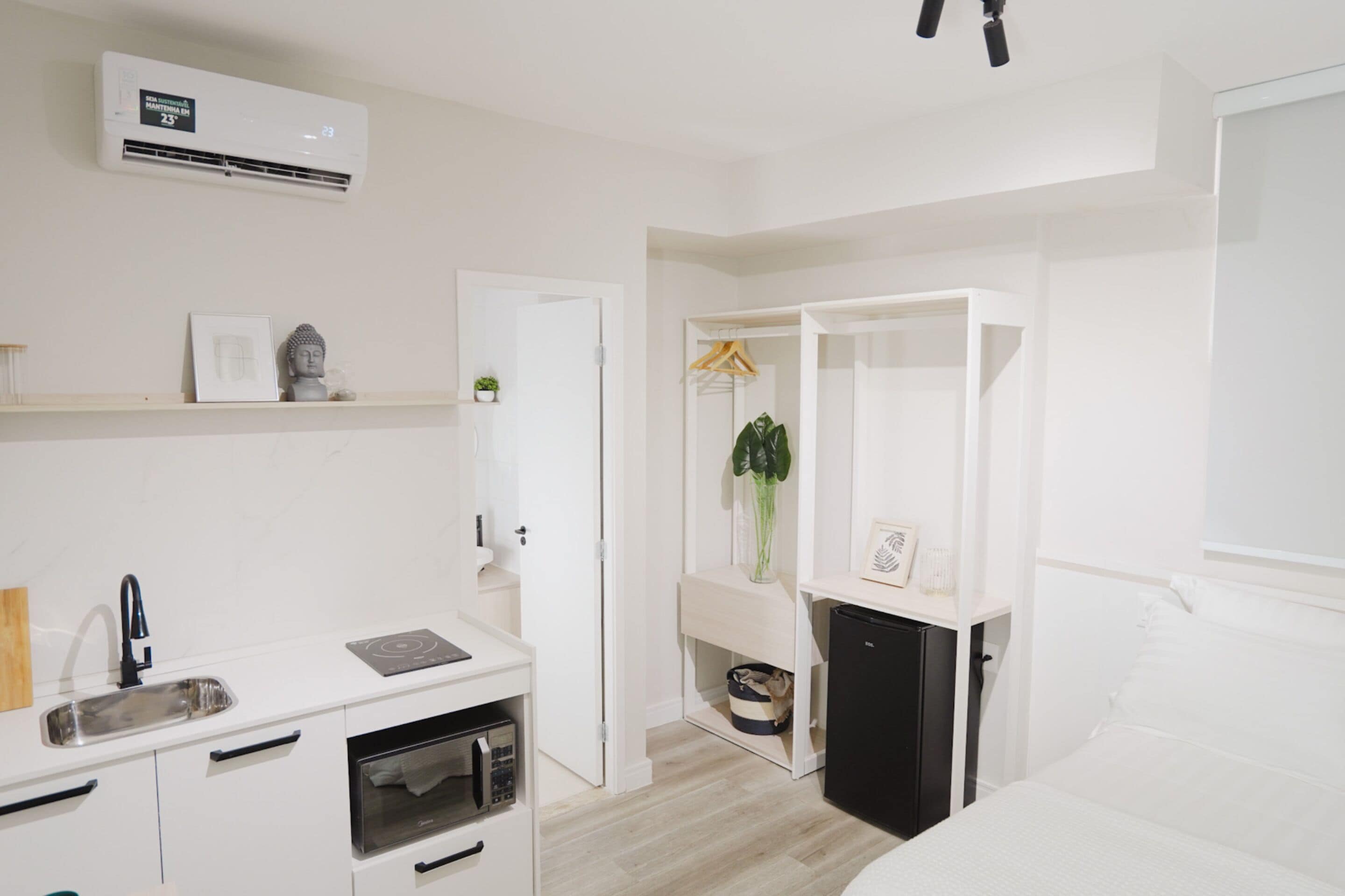 Une chambre à coucher moderne, décorée dans des tons de blanc, comprenant un lit, une table de chevet, une armoire et un petit coin cuisine.