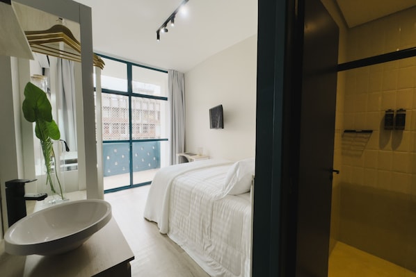 A modern bedroom with a large window, a bedside table, and a shower area. - Apê Metrô Paraíso (São Paulo)