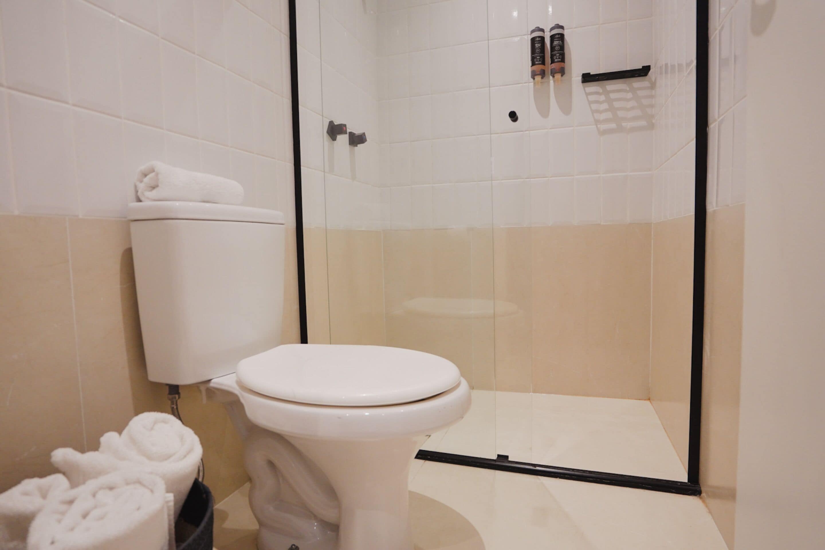 A bathroom with a toilet, a glass shower enclosure, and a towel rack with towels.
