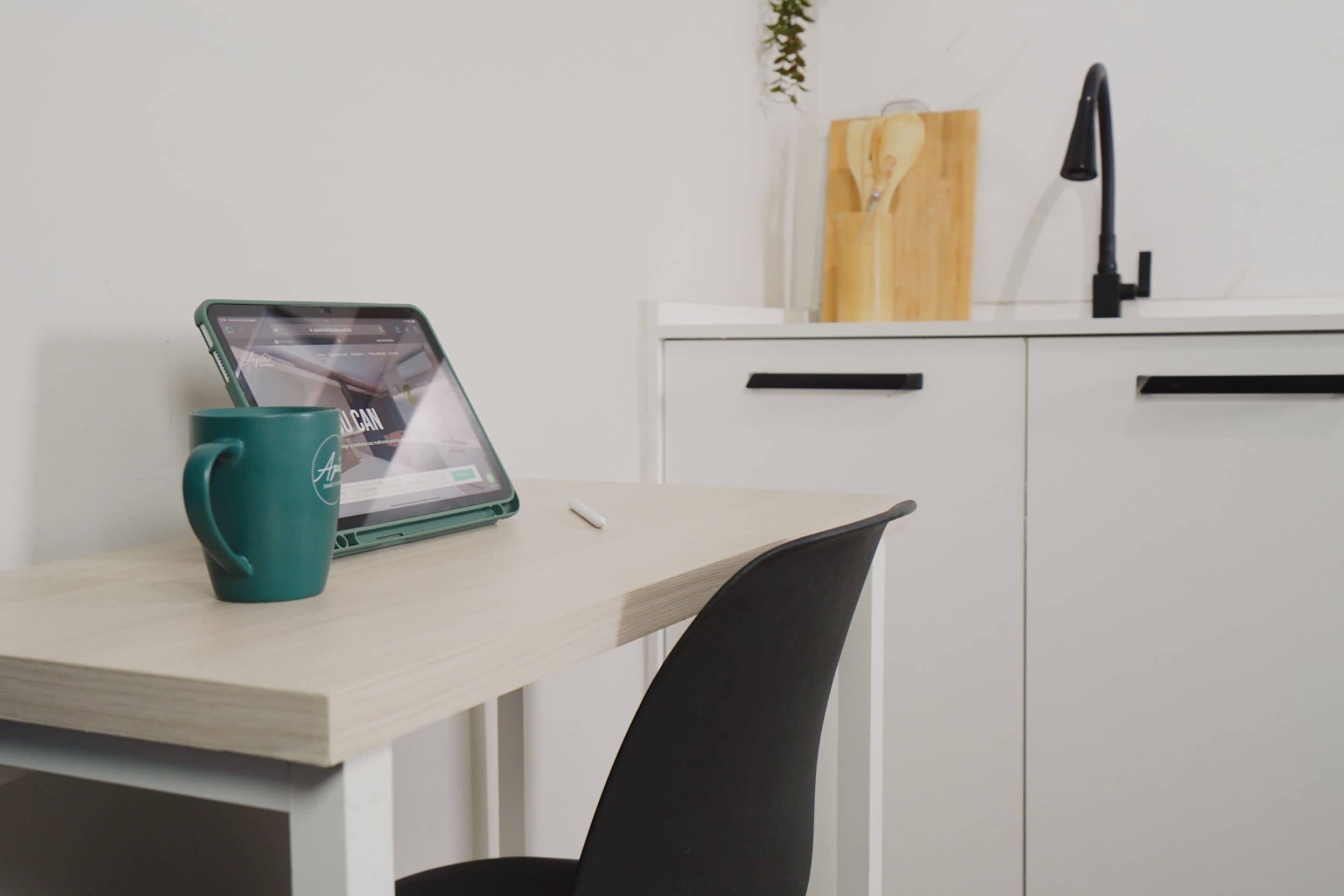 Eine moderne Küche mit einem Holztisch, einer blaugrünen Tasse, einem Tablet und einem schwarzen Stuhl.