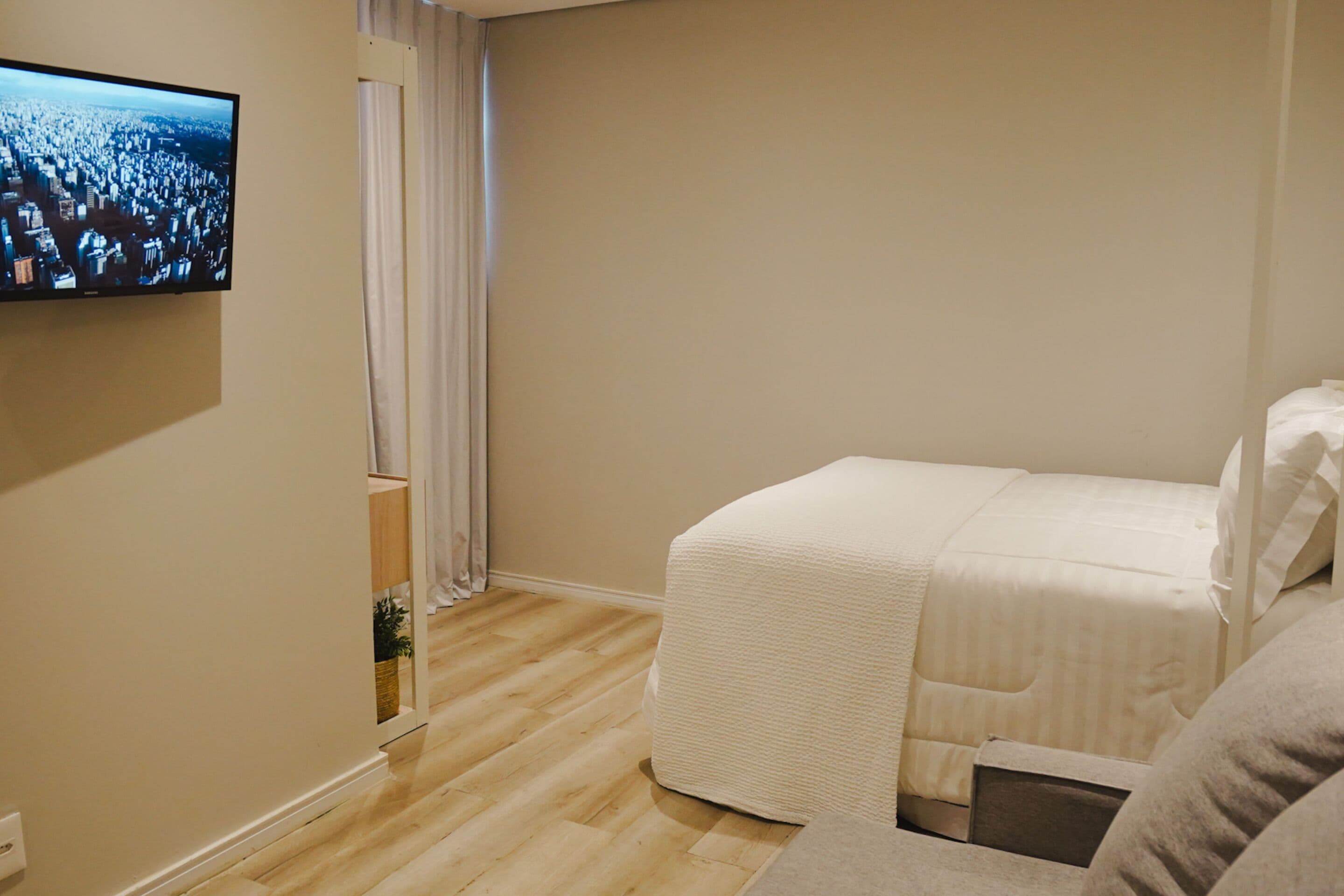 Ein Hotelzimmer mit einem Bett, einem an der Wand montierten Fernseher und einem Holzboden.