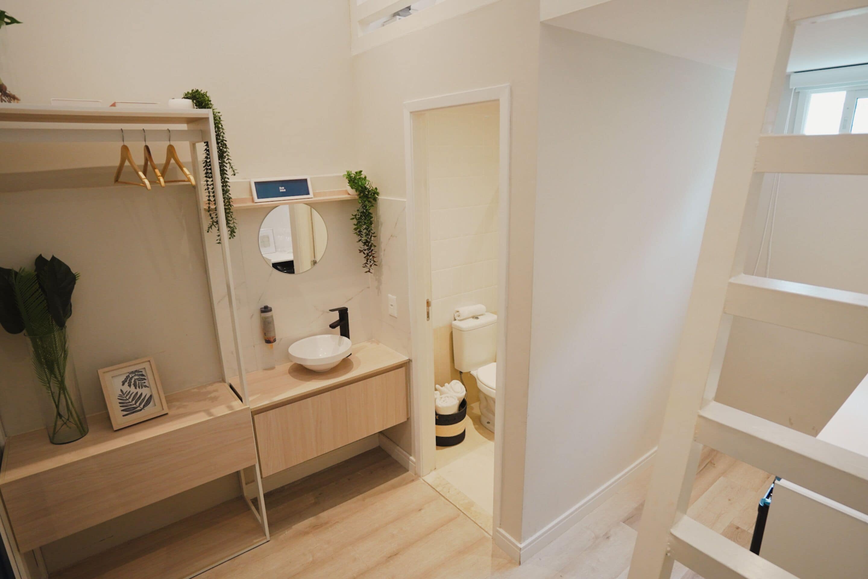 Un baño moderno con tocador de madera, un espejo redondo, un inodoro y un estante pequeño con plantas.