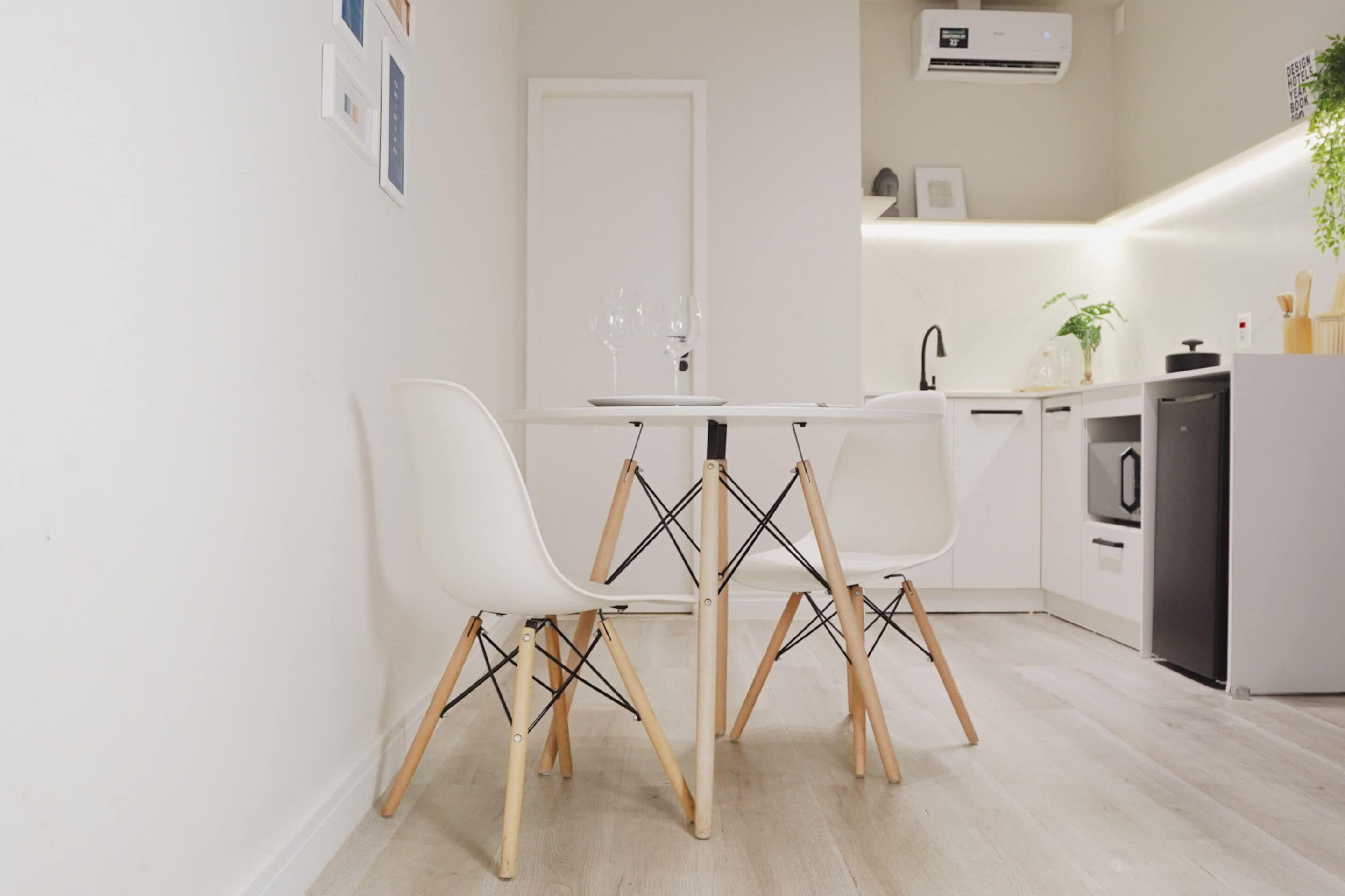 A modern kitchen with white cabinetry, a built-in oven, and a dining area with two white chairs and a white table.