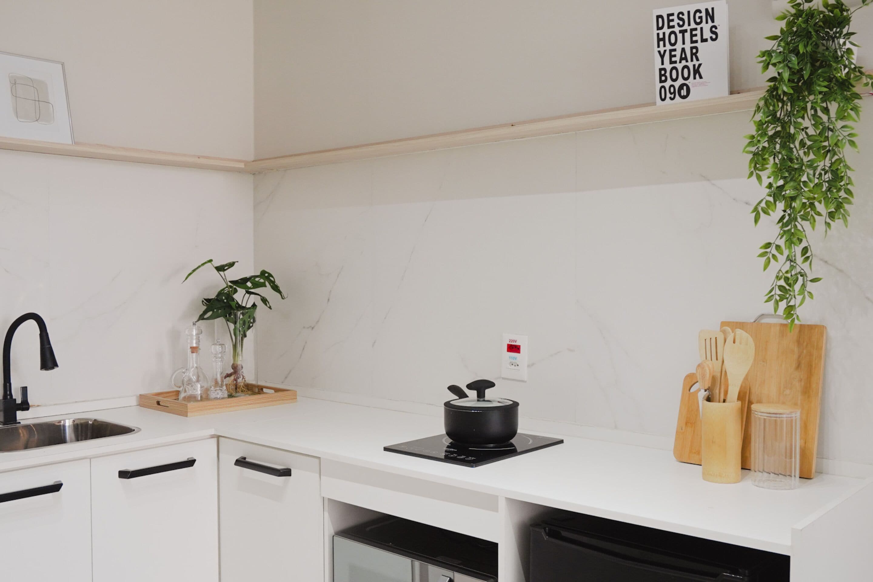 Une cuisine moderne dotée d’un plan de travail blanc, d’une plaque de cuisson à induction noire, d’un évier et d’une planche à découper en bois avec des ustensiles.