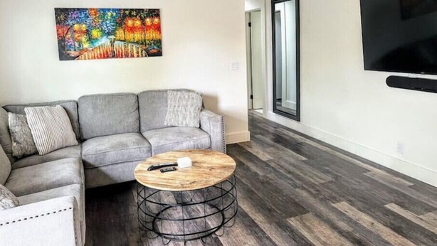 Un salon avec un canapé d’angle gris, une table basse ronde dotée d’un pied en métal et un tableau abstrait aux couleurs vives accroché au mur.