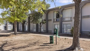 A building with a courtyard, trees, and a green trash bin. - Studio 6 Pecos, Tx (Pecos)
