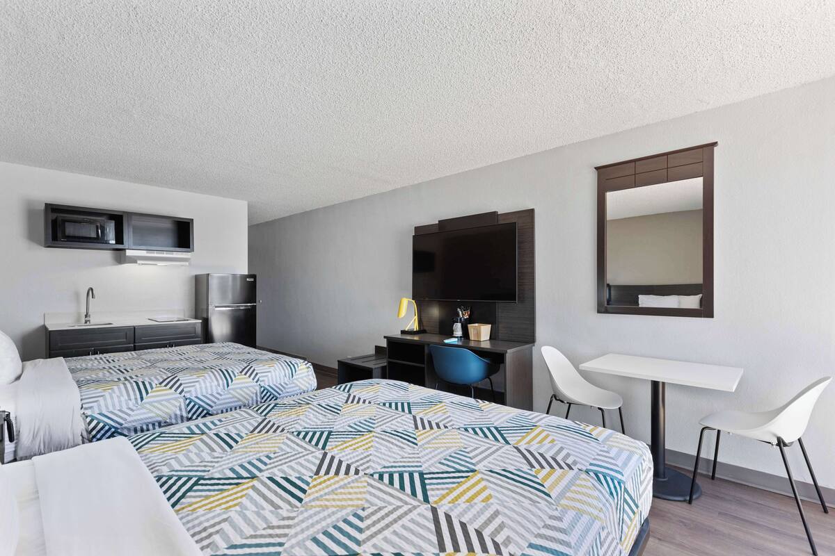 A hotel room with two beds, a desk, a chair, a mirror, a TV, and a microwave.