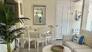 A living room with a round coffee table, white sofas, a dining table with chairs, and a potted plant. - FLAMINGO COTTAGE summer fun. Pool, boating, fishing lobster season.  (Summerland Key)