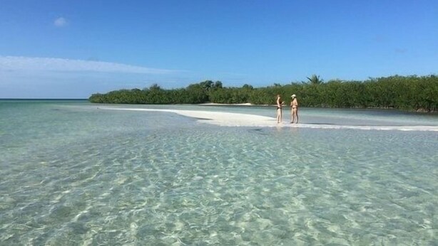 A beach with clear shallow waters and a sandy area where two people are standing. - FLAMINGO COTTAGE summer fun. Pool, boating, fishing lobster season.  (Summerland Key)
