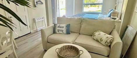 Uma sala de estar moderna com um sofá bege, uma mesa de centro redonda com um objeto decorativo tecido e uma grande janela com vista para o exterior.