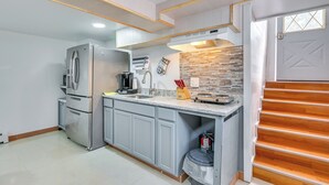 Une cuisine moderne avec des meubles gris, un réfrigérateur en acier inoxydable, un four encastré et un escalier en bois menant à une porte dotée d’une fenêtre.