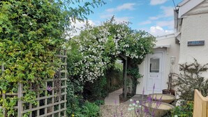 Un sentier de jardin menant à une porte blanche, entourée d’une végétation luxuriante et de plantes en fleurs.