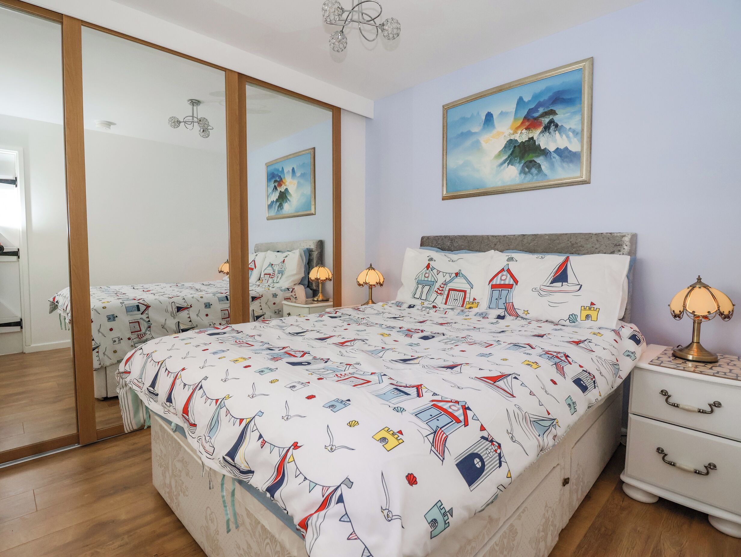 A bedroom with a large bed, two bedside tables, a nightstand, a mirror, and a painting on the wall.