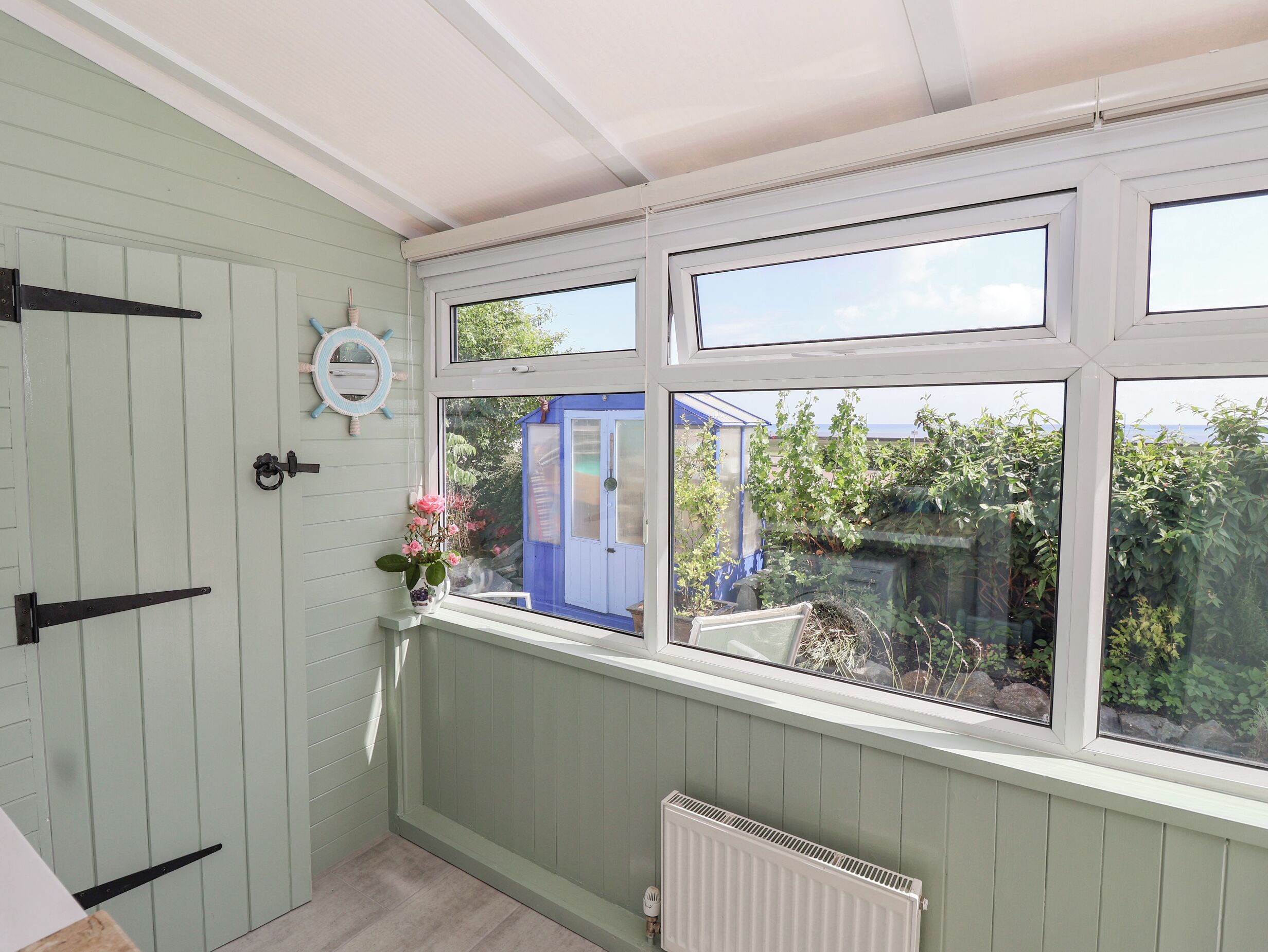 A room with a view of a garden, a blue door, and a white radiator.