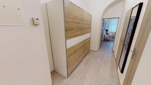 Un couloir avec un mur recouvert de panneaux de bois, une porte dotée d’une poignée noire et un interrupteur sur le mur.