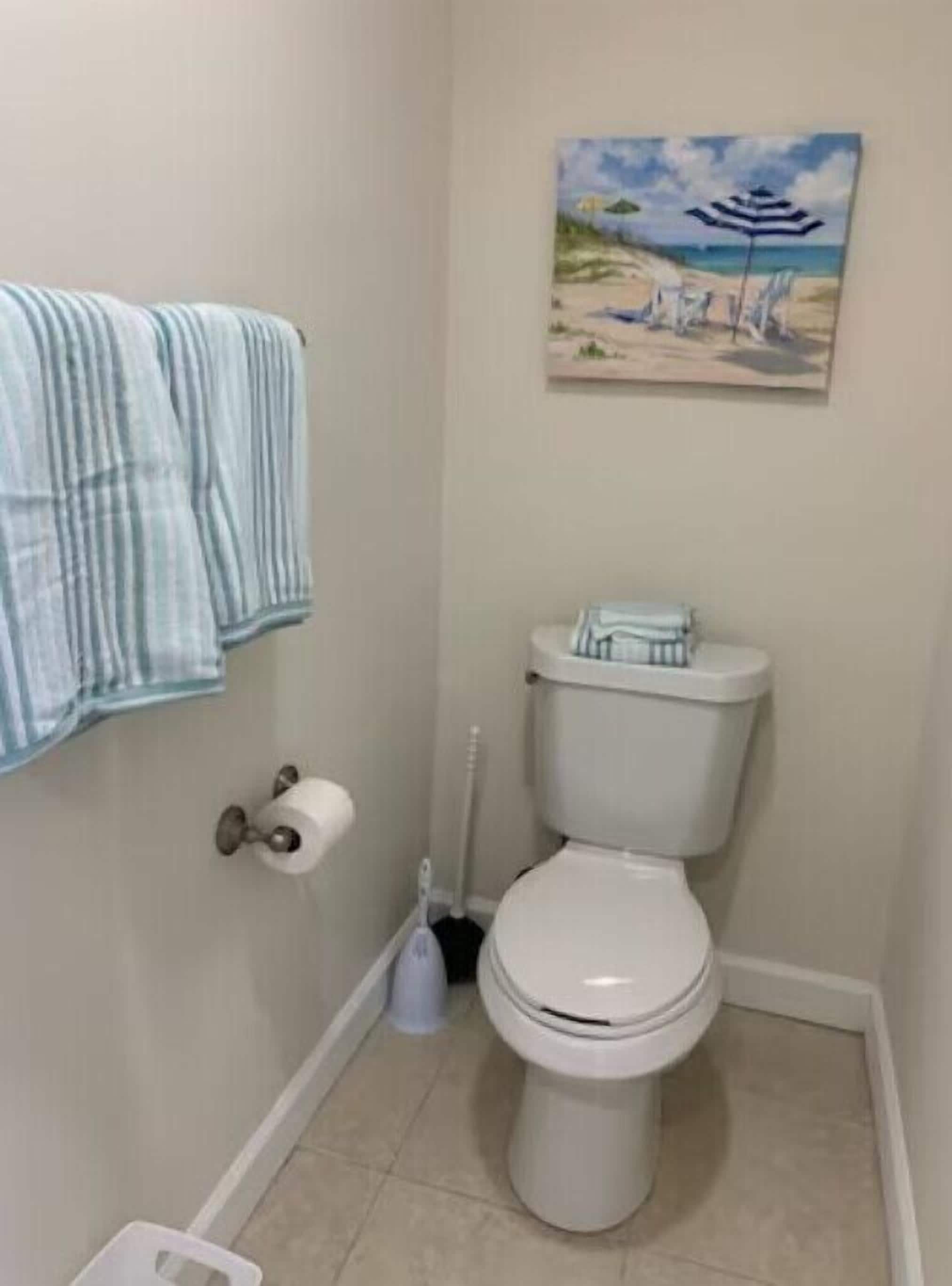 Un baño con inodoro, un rollo de papel higiénico, un cepillo de limpieza y una toalla colgada en la pared.