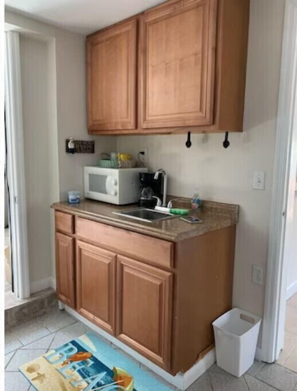 A kitchen with wooden cabinets, a microwave, a sink, and a trash bin. - SEA SHELL COTTAGE, Perfect for 2 guests (Summerland Key)