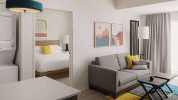 A modern hotel room with a bed, sofa, and a small table. There is a window with curtains, a wall-mounted lamp, and artwork on the wall.
