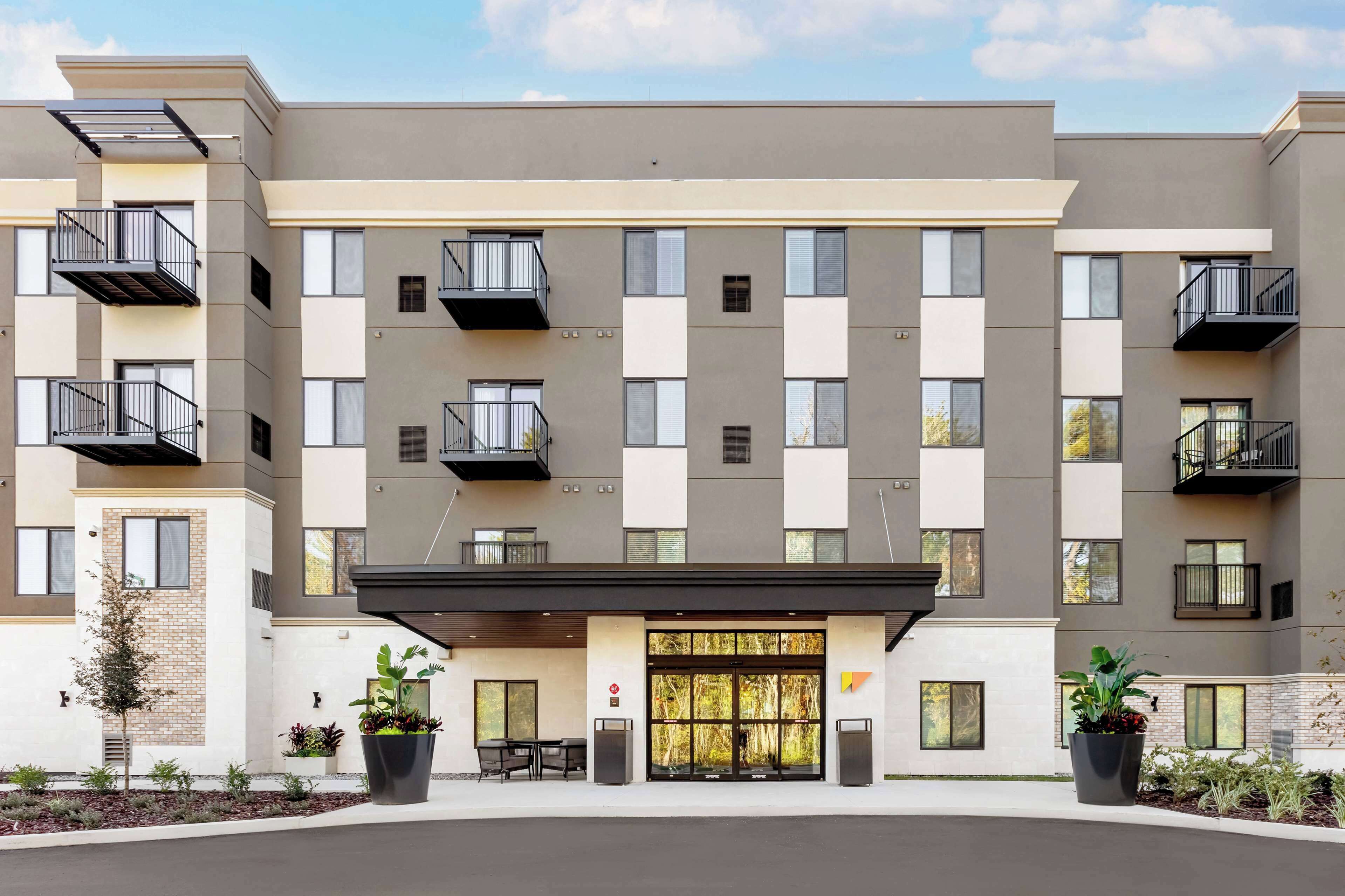A multi-story building with balconies, a central entrance, and outdoor seating.