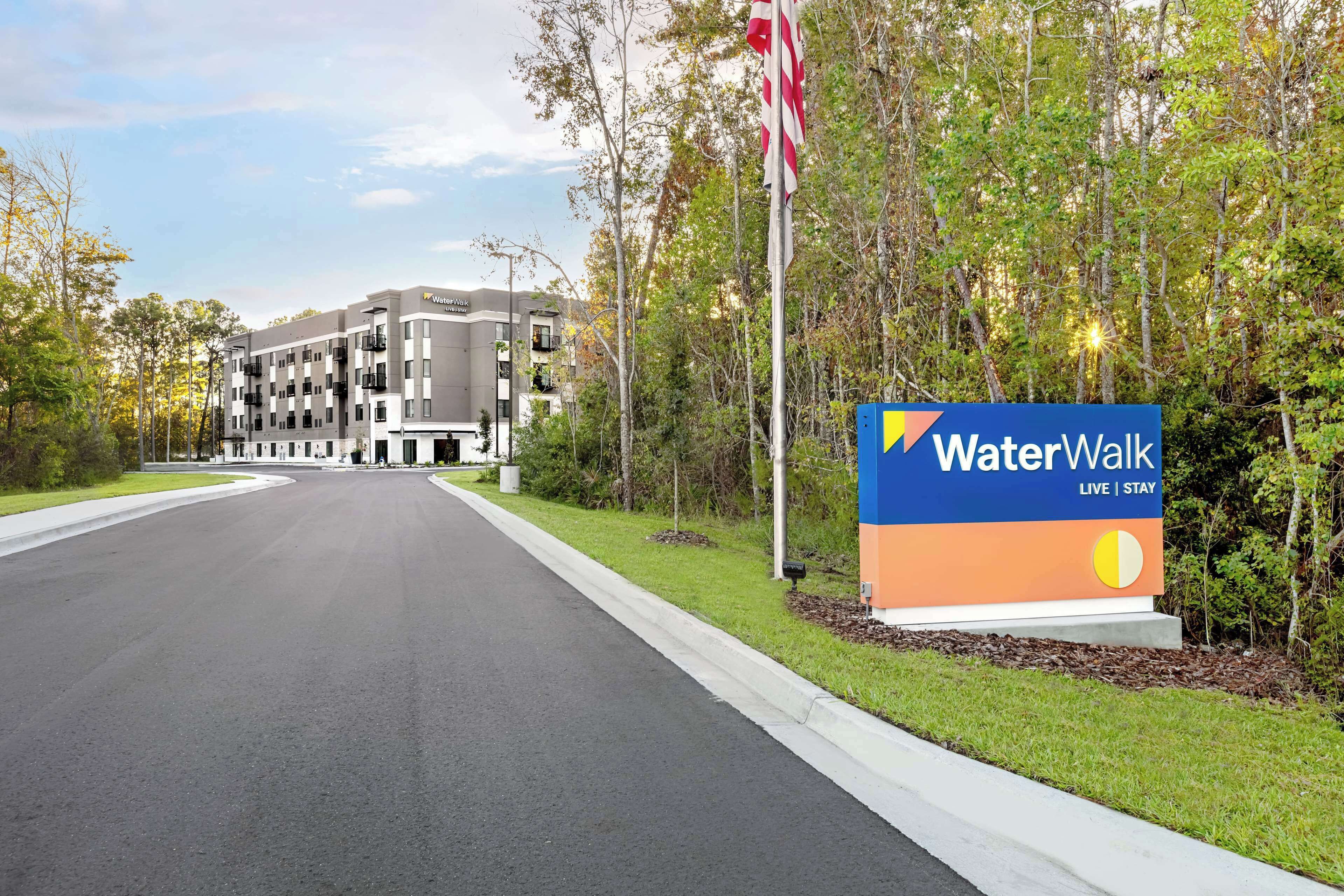 Eingang eines WaterWalk Hotels mit Schilder, einer Flagge und einem Gebäude im Hintergrund.