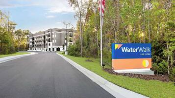 Entrada de un hotel WaterWalk, con un letrero, una bandera y un edificio al fondo.