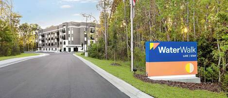 A WaterWalk hotel entrance with a sign, a flag, and a building in the background.