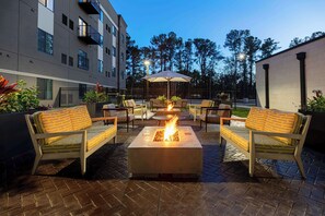 An outdoor patio with a fire pit, seating, and a view of a building in the background.