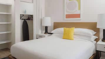 Habitación de hotel con una cama bien hecha, un armario, una lámpara y una obra de arte en la pared.
