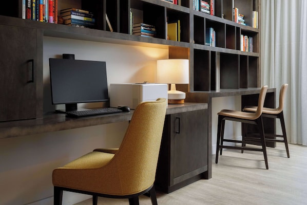 A modern workspace with a desk, computer, and two chairs, a bookshelf with books, and a lamp.