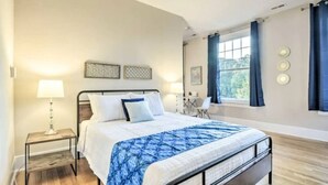 A bedroom with a bed, bedside table, lamp, and a window with curtains. - Historic 1925 Apt Near Downtown! (Raleigh)