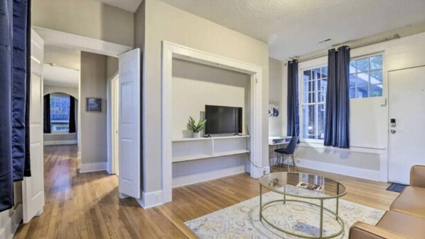 A modern living room with a glass coffee table, wooden flooring, and built-in shelving. - Historic 1925 Apt Near Downtown! (Raleigh)