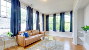 A spacious living room with a beige sofa, a glass coffee table, and a patterned rug. - Historic 1925 Apt Near Downtown! (Raleigh)