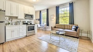 A modern kitchen with white cabinets, a microwave, and an oven. There is a beige sofa with a glass coffee table in the living area. - Historical 1BR Apt in Glenwood (Raleigh)