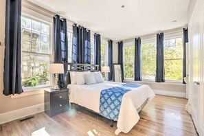 A spacious bedroom with a large bed, dark curtains, and a view of greenery outside. - Historical 1BR Apt in Glenwood (Raleigh)