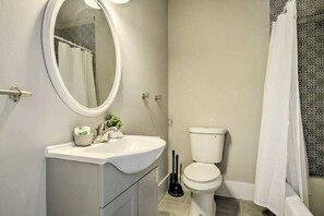 A bathroom with a white sink, mirror, toilet, and shower curtain. - Historical 1BR Apt in Glenwood (Raleigh)