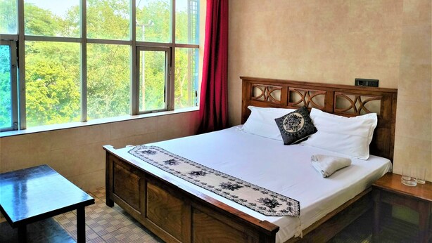 Ein Hotelzimmer mit großem Fenster, einem Bett mit weißer Bettwäsche, einem Holzkopfstück und einem kleinen Tisch.