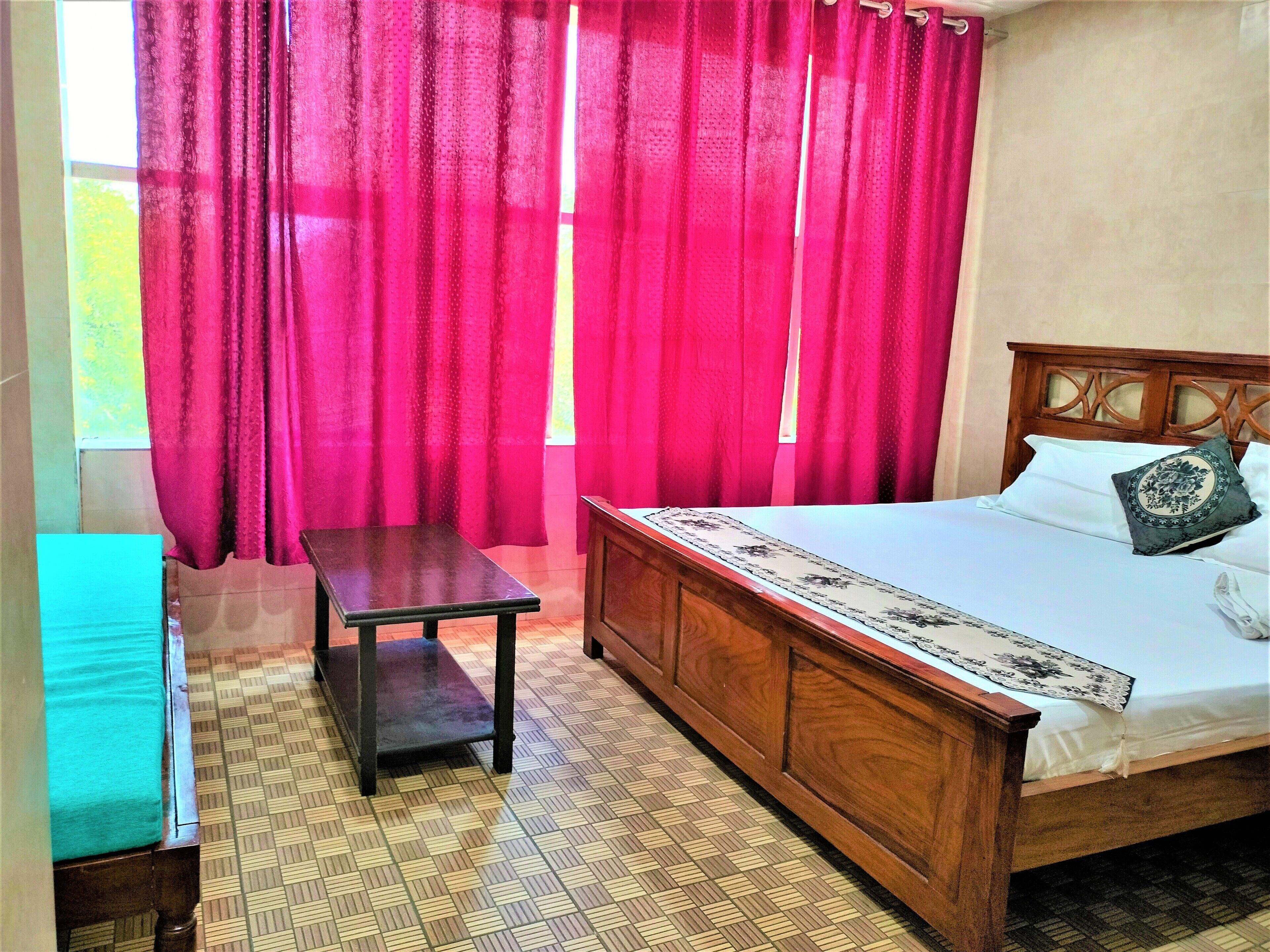Une chambre à coucher avec un lit en bois, une petite table et une fenêtre ornée de rideaux rouges.