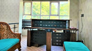 Ein Zimmer mit Schreibtisch, zwei Stühlen, einem Fenster mit Blick auf Bäume und Wandverkleidung mit Muster.