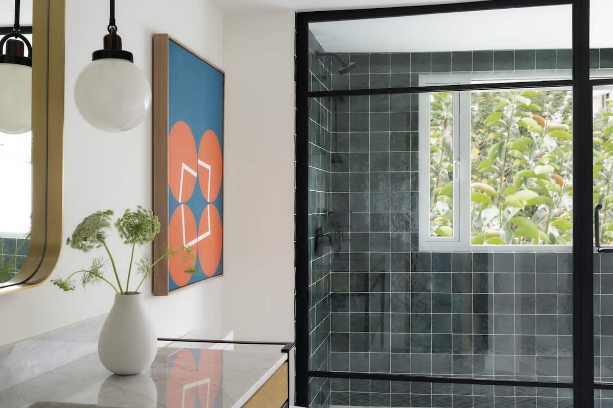 A modern bathroom with a glass shower enclosure, a white toilet, and a large window offering a view of greenery.